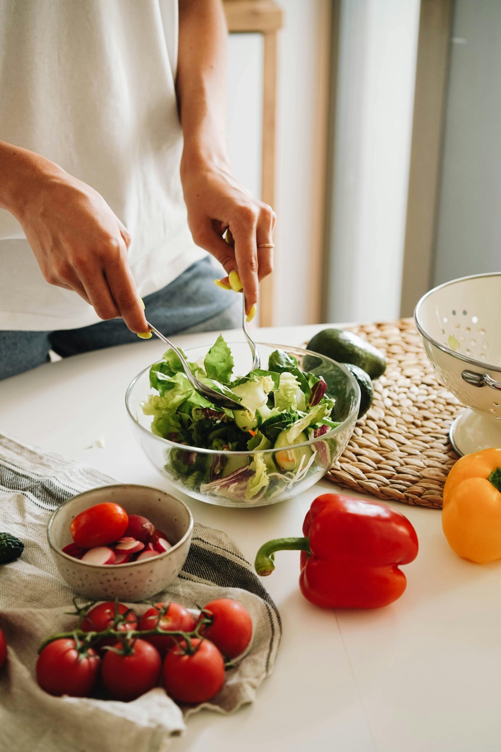 A person mixes a fresh vegetable salad with tomatoes and bell peppers in a kitchen.